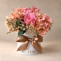 Promessa di Rosa: cinque rose rosa e ortensie pesca stabilizzate in cappelliera bianca con fiocco satinato caramello.