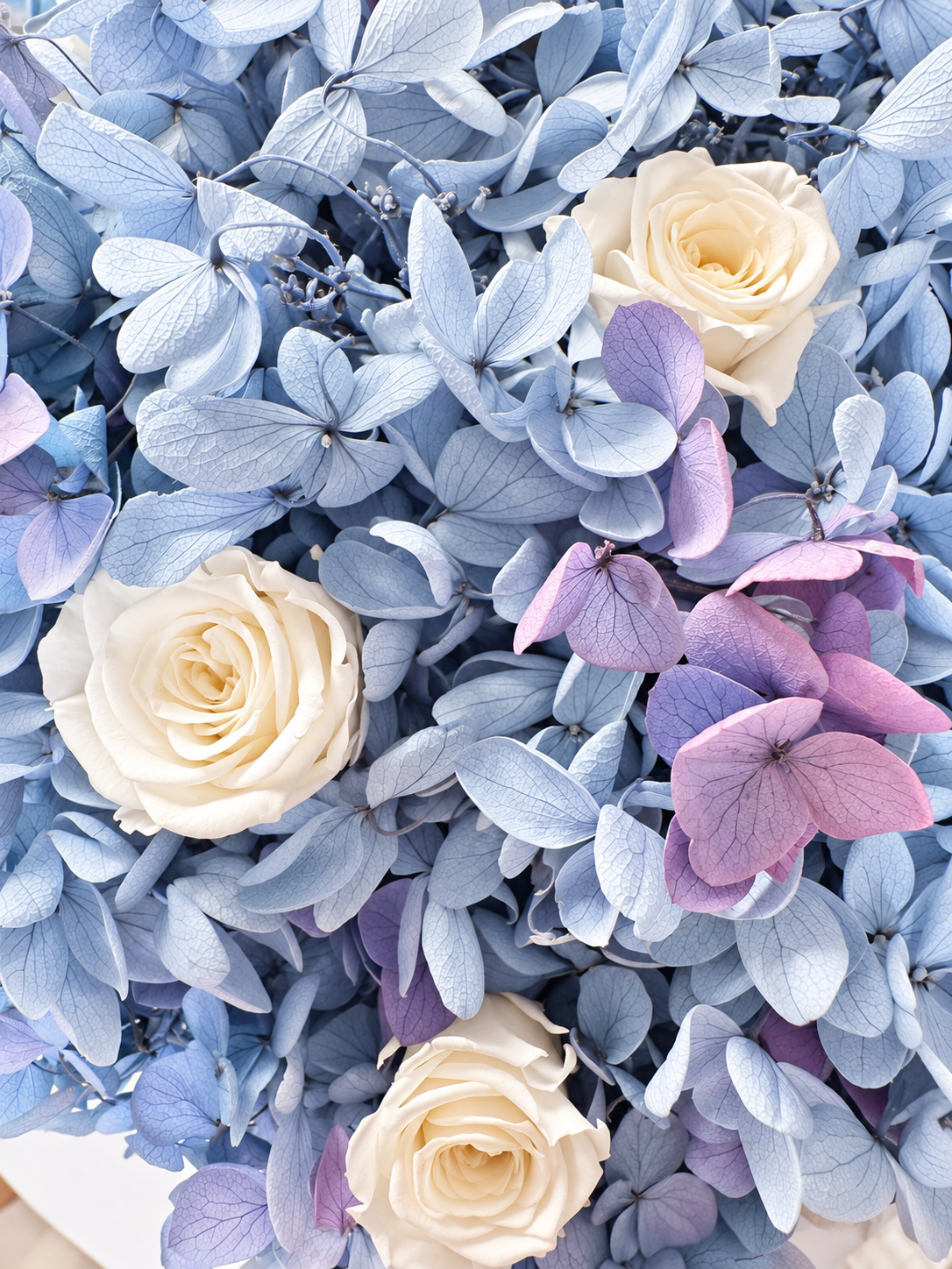 Dettaglio di Brezza Marina: rose avorio e petali di ortensie azzurre e malva stabilizzate.