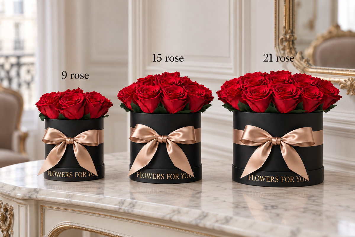 Tre bouquet di rose rosse stabilizzate da 9, 15 e 21 rose in scatole nere con fiocchi champagne, affiancati su una consolle in marmo.