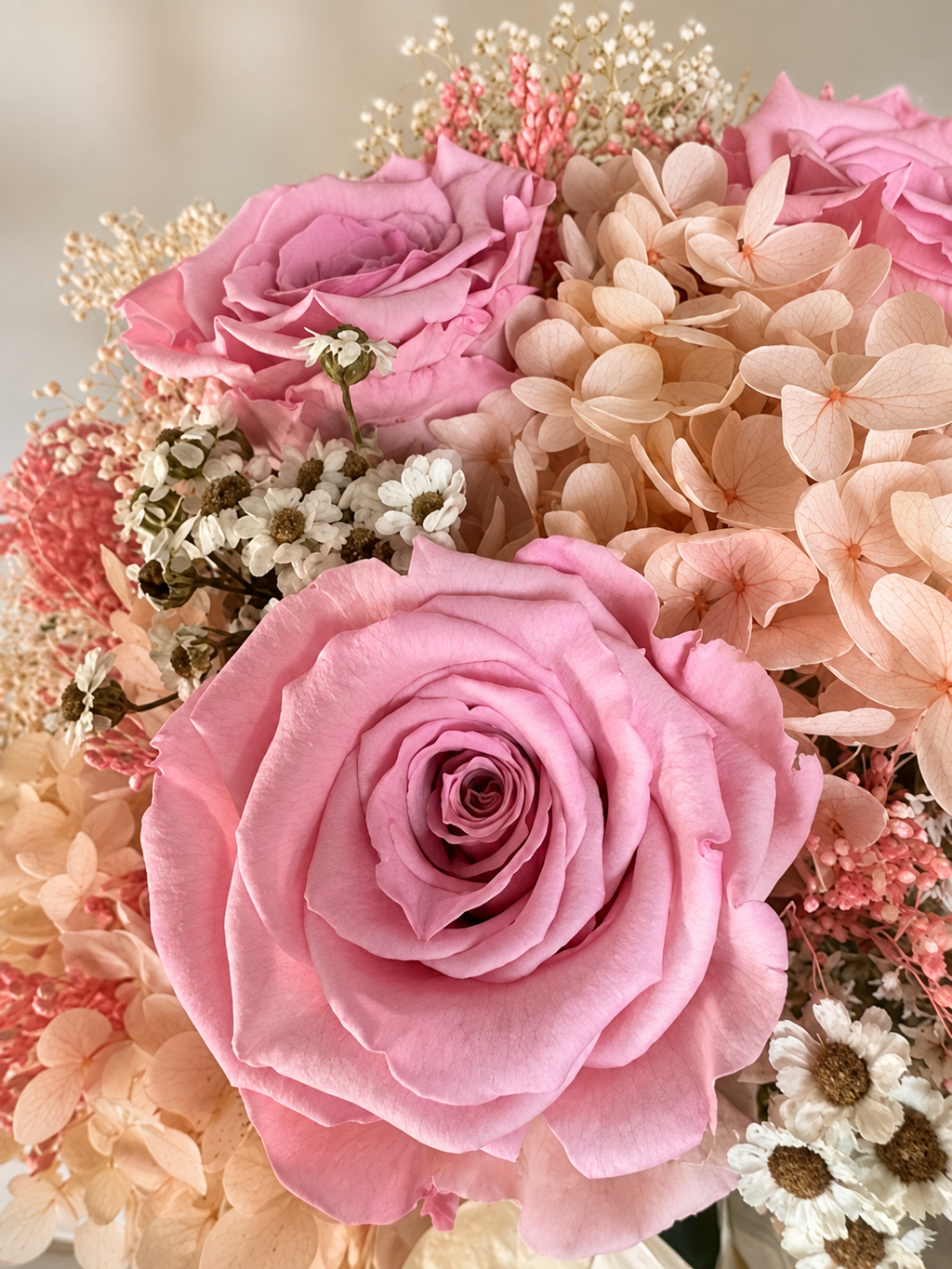 Primo piano delle rose rosa stabilizzate di Promessa di Rosa con ortensie pesca e margherite.