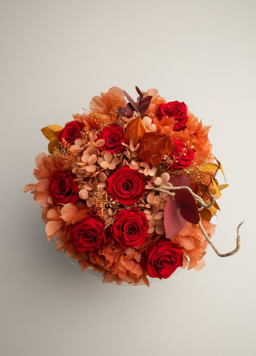 Amaranto visto dall’alto: rose rosse e ortensie terracotta stabilizzate con rametti decorativi.