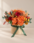Velluto d'Autunno: ortensie arancio, rose rosse ed eucalipto stabilizzati in cappelliera in velluto sabbia con fiocco verde bosco, su fondo avorio.