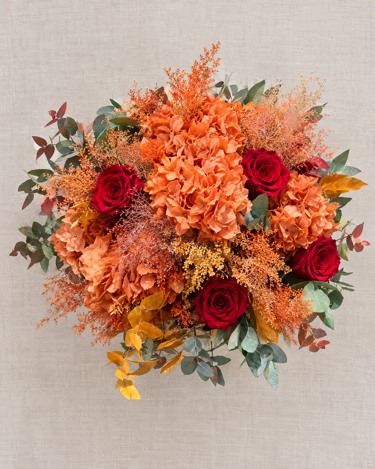 Velluto d'Autunno vista dall’alto: quattro rose rosse tra ortensie arancio, spighe ramate, foglie senape ed eucalipto.