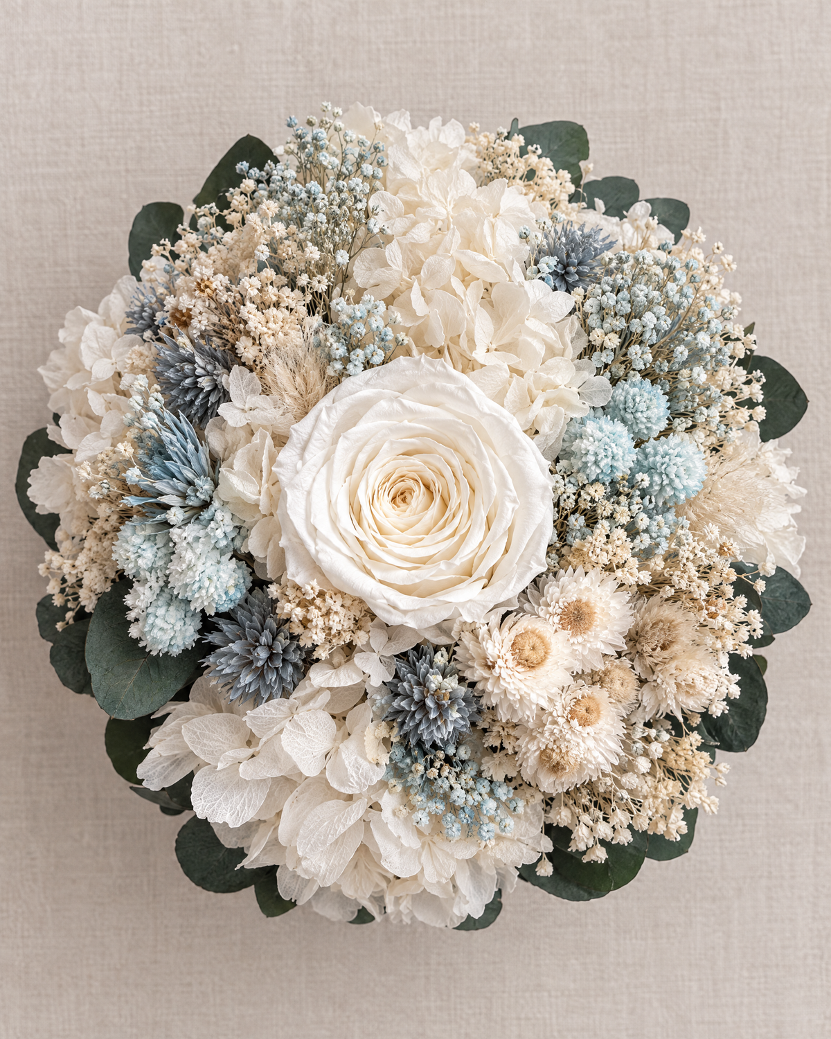 Velo Celeste vista dall’alto: rosa avorio al centro tra ortensie bianche, elicrisi crema, gypsophila e accenti azzurri.