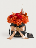 Amaranto: ortensie terracotta e rose rosso intenso stabilizzate in cappelliera nera con fiocco champagne e sigillo in ceralacca dorata.