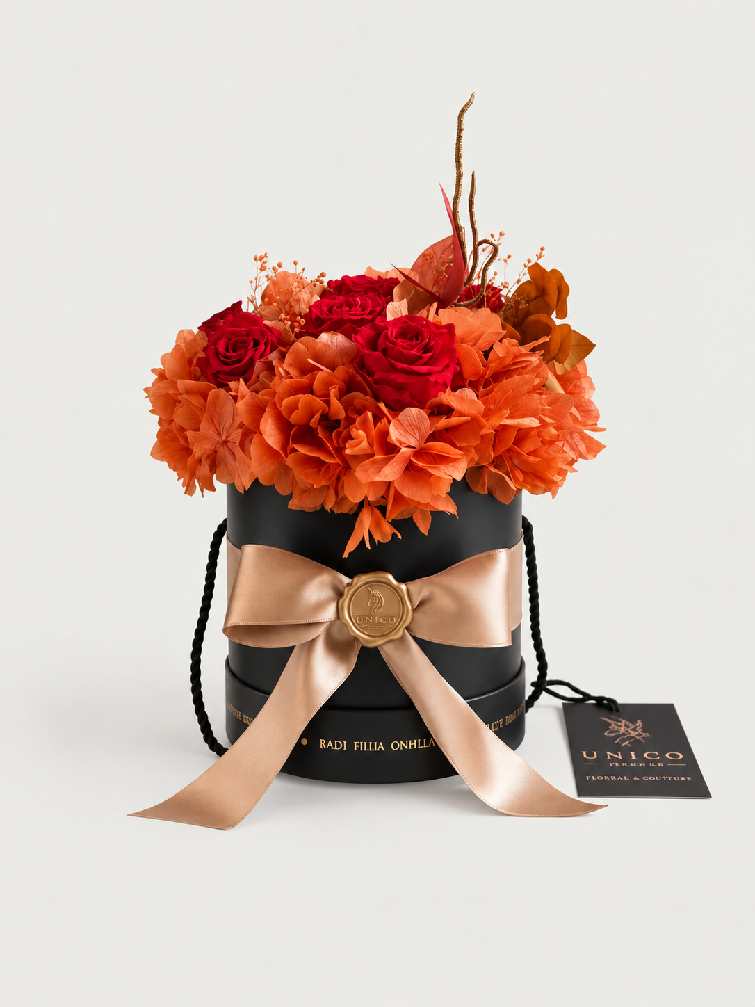 Amaranto: ortensie terracotta e rose rosso intenso stabilizzate in cappelliera nera con fiocco champagne e sigillo in ceralacca dorata.