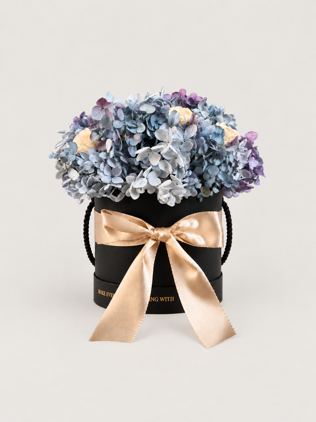 Brezza Marina: ortensie azzurre e malva con rose avorio stabilizzate in cappelliera nera con fiocco champagne.