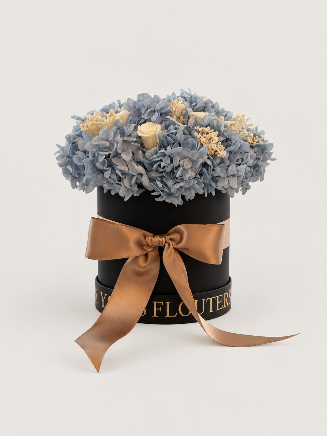 Cielo di Seta: ortensie azzurro polvere e rose avorio stabilizzate in cappelliera nera con fiocco satinato caramello.