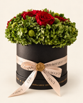 Rosso Bosco: rose rosse e ortensie verdi in cappelliera nera con nastro champagne e sigillo dorato, su fondo avorio.