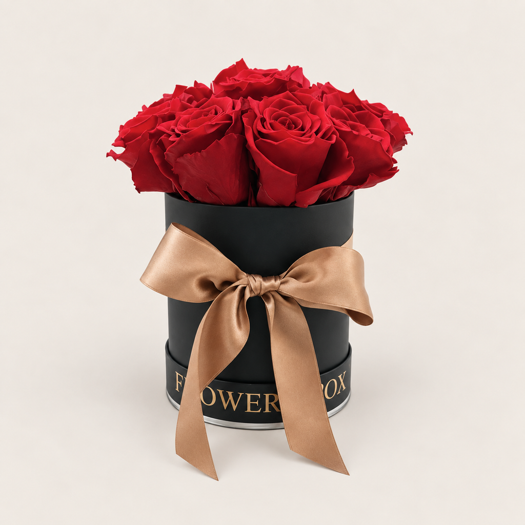 Rosso di Seta: nove rose rosse stabilizzate in scatola cilindrica nera con fiocco satinato champagne, su fondo avorio.