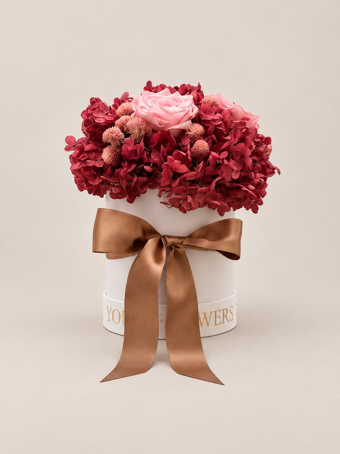 Rubino Rosé: ortensie rosso rubino e rose rosa stabilizzate in cappelliera bianca con fiocco satinato caramello.