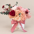 Sussurro di Cipria: rose rosa e bordeaux, ortensie cipria ed eucalipto in cappelliera bianca con fiocco rosa antico.