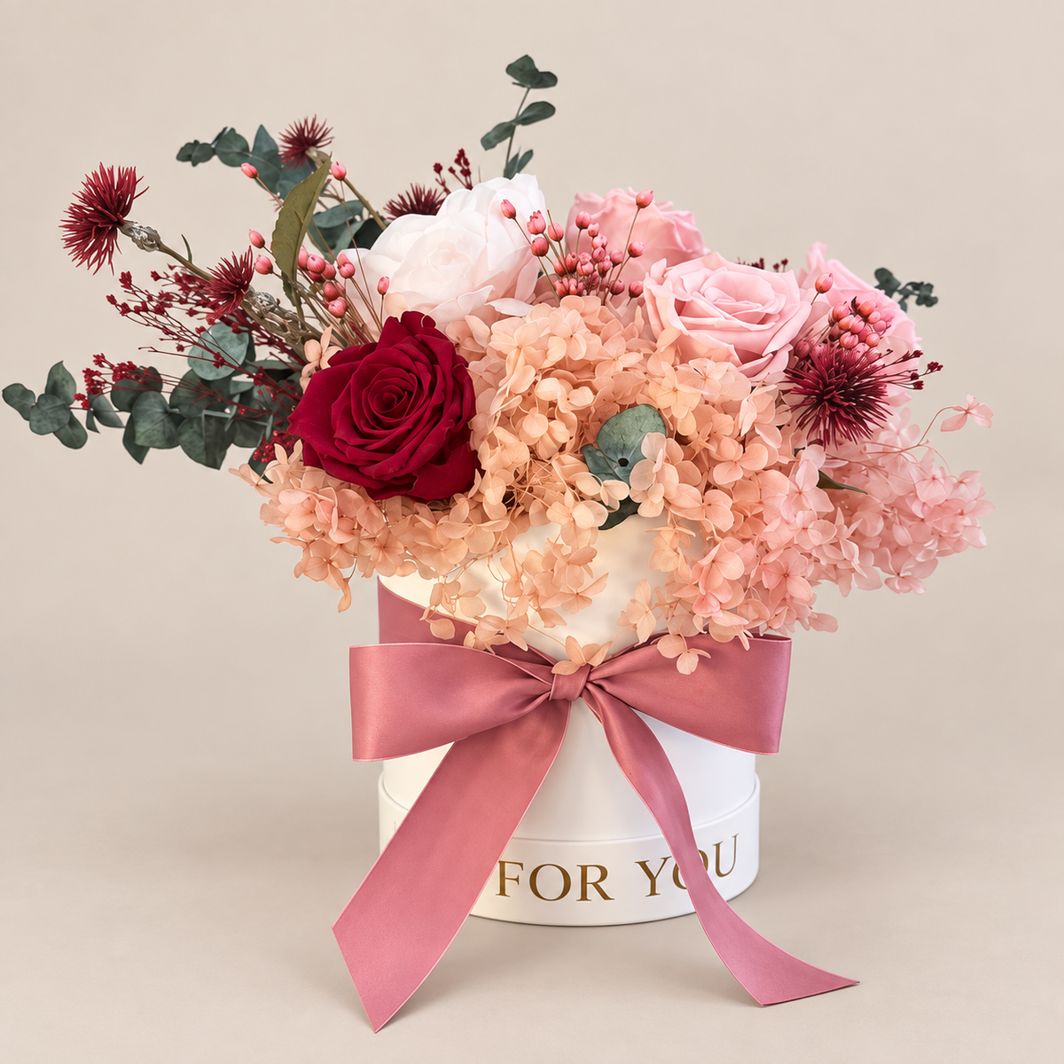 Sussurro di Cipria: rose rosa e bordeaux, ortensie cipria ed eucalipto in cappelliera bianca con fiocco rosa antico.