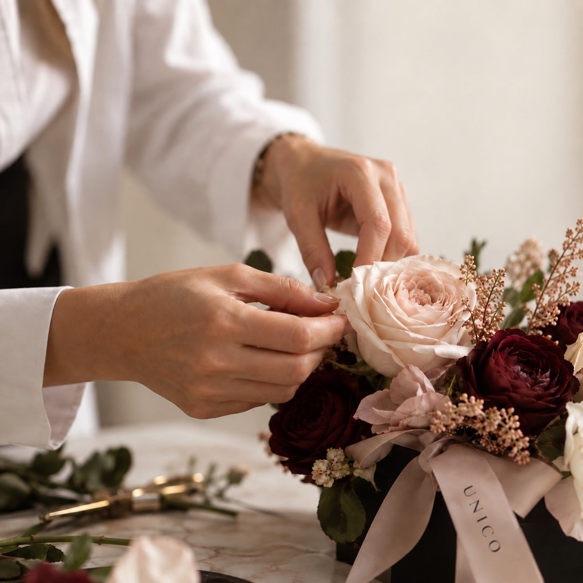 Mani che curano una composizione di rose rosa cipria e bordeaux